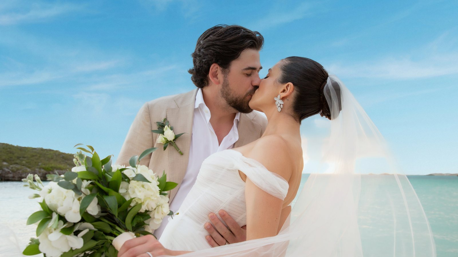 A bride and groom kissing on a Turks and Caicos beach, her veil catching the wind